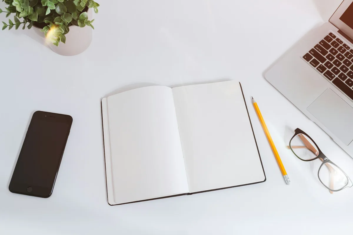 Open notebook beside a laptop and stationery on a light desk